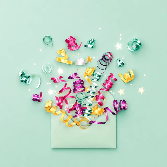Confetti and streamers bursting out of an opened birthday card envelope
